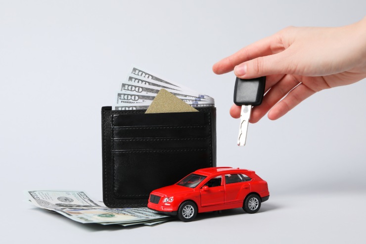 Auto giocattolo, persona che tiene le chiavi e un portafoglio pieno di banconote